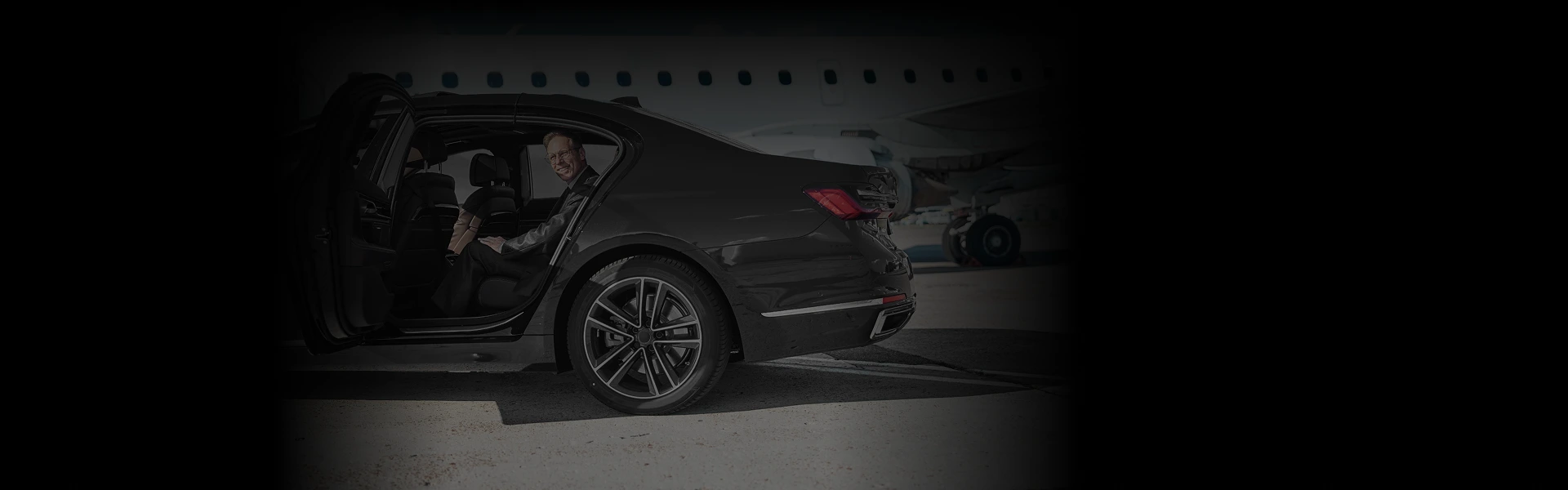 Baltimore Airport Car Service showing a luxury black sedan side-angle with smiling passenger seated inside near aircraft background.